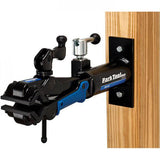 Park Tool PRS-4W-2 Deluxe Wall-Mount Bike Repair Stand with 100-3D Clamp, mounted on workshop wall for bike maintenance.