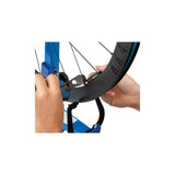 Park Tool CSH-1 clamping spoke holder for wheel truing and spoke tensioning, shown in a workshop setting with bike wheels.