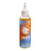 Joe's No Flats PTFE Dry Lube applied to a bicycle chain and drivetrain for smooth, dry lubrication in workshop setting.