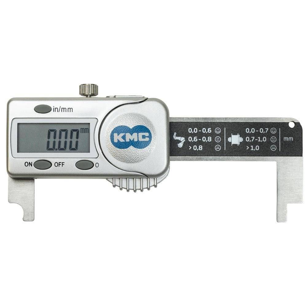 KMC digital bike chain checker tool used for measuring chain wear, shown on a workshop workbench with bike components.