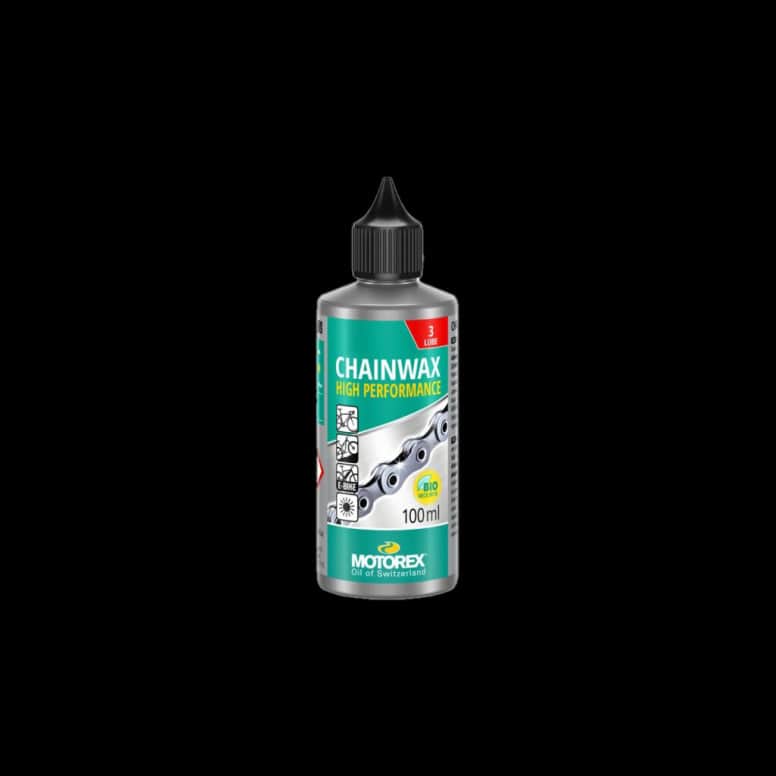 Motorex Chainwax bicycle chain lubricant in 100ml silver-green bottle with durable wax film, shown in a workshop setting.