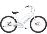 Electra Cruiser Go! Step-Thru e-hybrid bike with pedal assist and flat foot technology, shown outdoors with a city background.