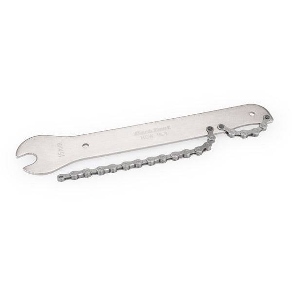 Park Tool HCW-16.3 chain whip and 15mm pedal wrench for bike maintenance, shown in a workshop setting with tools and bike parts.