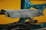 Gtechniq Bike Premium Microfibre Cloth triple pack for bike cleaning and maintenance, shown in a workshop setting.