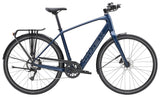 Trek FX+ 2 LT e-hybrid commuter bike with pedal assist, rear rack, and disc brakes, shown in a city street setting.