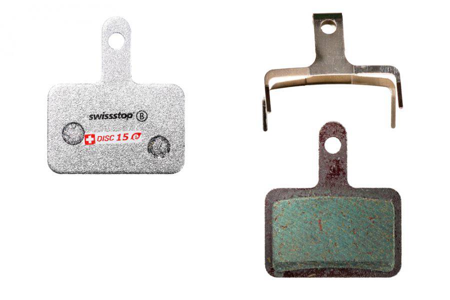SwissStop Disc 15 brake pads for Shimano M5, T6, and M3 silver disc brakes, shown installed on bicycle wheel.