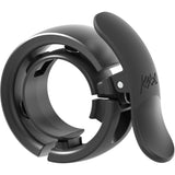 Knog Oi Prima bike bell with Wave-Tek technology and cable management, mounted on a bicycle handlebar, showcasing sleek design.