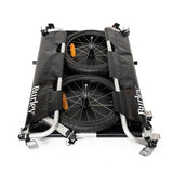 Burley flatbed cargo bike trailer with foldable two-wheel design for bulk hauling, shown attached to a bicycle in outdoor setting.