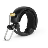 Knog Oi Luxe large bike bell in matte black with clear, resonant sound mounted on a bicycle handlebar.