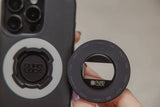 Quad Lock MAG phone ring stand with magnetic grip and bottle opener accessory, black and silver, attached to a smartphone.