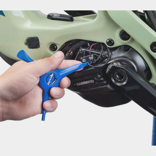 Park Tool EWS-2 electronic wire tool for Shimano Di2 and SRAM battery covers, shown in a workshop setting with the tool in hand.