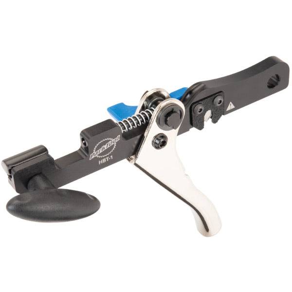 Park Tool HBT-1 hydraulic barb tool for brake hose cutting and installation, shown in a workshop setting with tools and work surface.