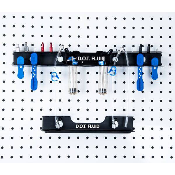 Park Tool JH-4 wall-mounted bleed kit organizer for hydraulic brake accessories in a workshop setting, with tools and accessories visible.