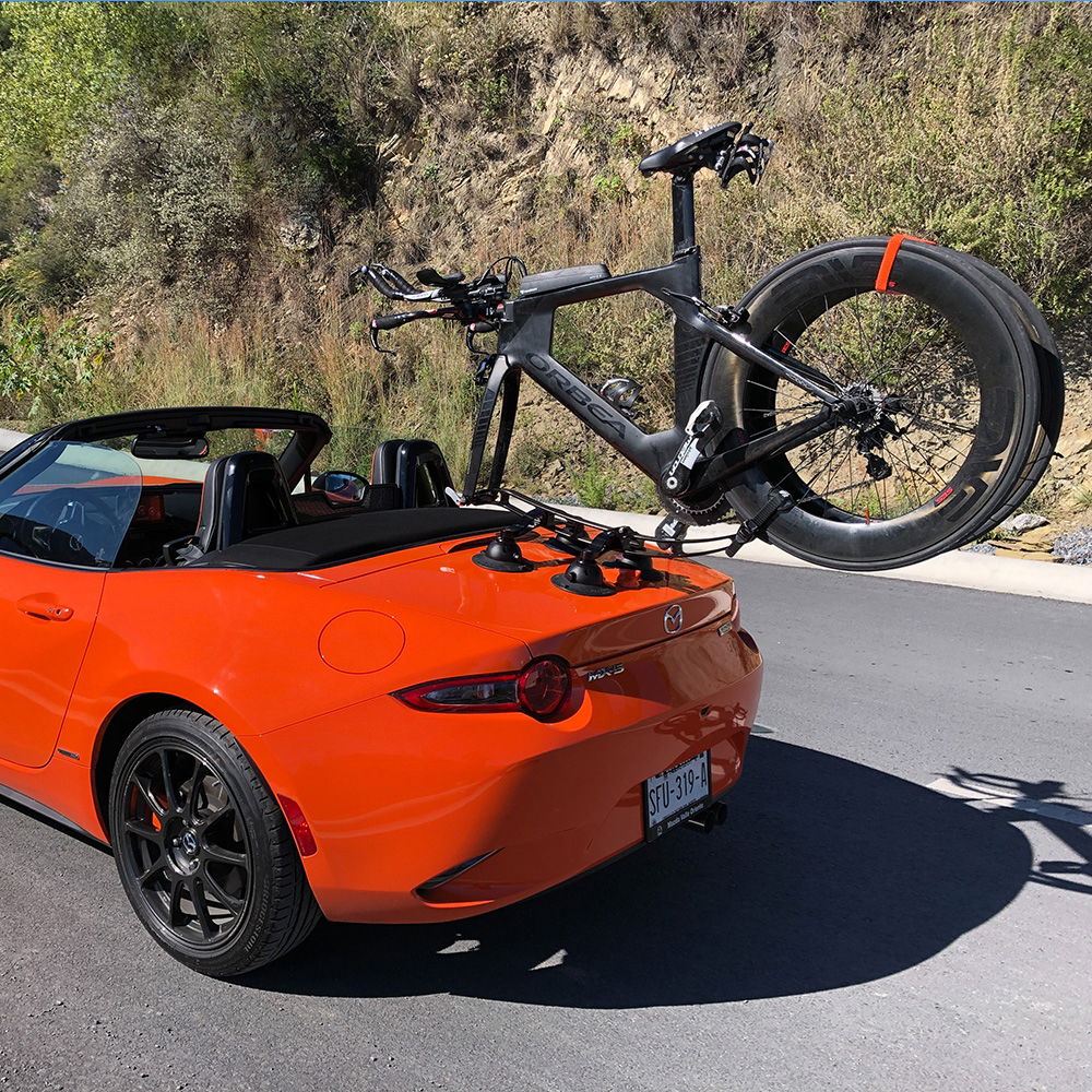 SeaSucker Komodo 1 bike rack mounted on a sports car roof, showcasing compact roof-mount design for bikes and accessories.
